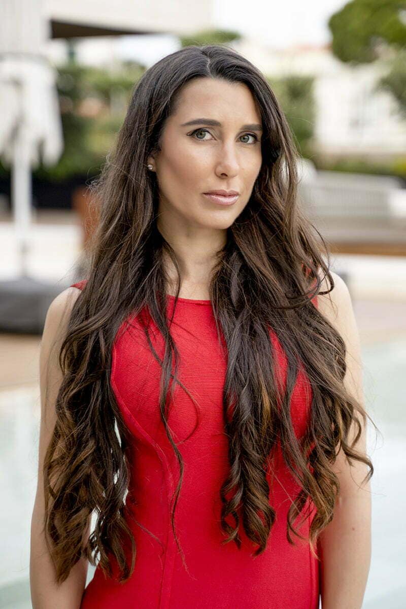 Woman in red dress posing outdoors near water.